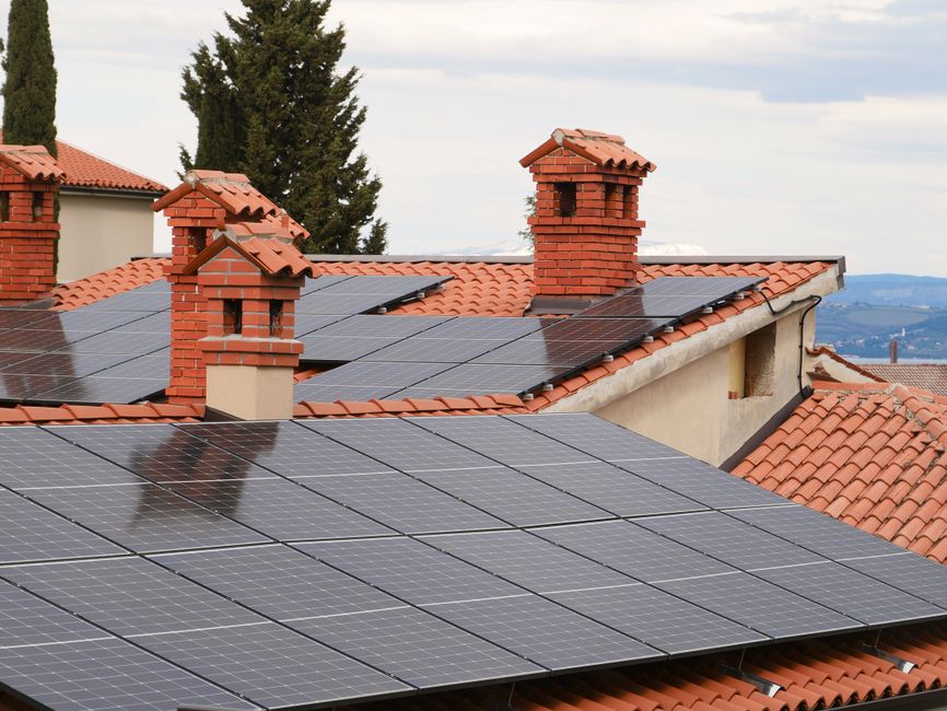 Solar panels on tiled roofs of houses with chimneys, capturing clean energy.