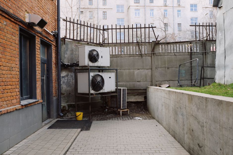 Contemporary building from brick with white air conditioning systems and yellow bucket in yard with fence and concrete wall in city