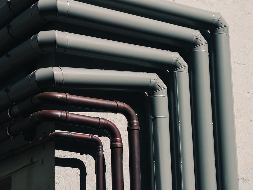 Close-up of industrial pipes forming a pattern on a building’s exterior wall, shot outdoors.