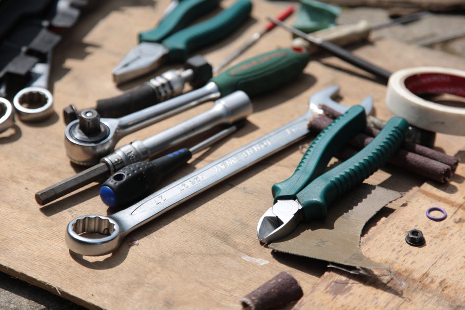 Close-up of various hand tools including pliers and a wrench placed on a wooden board.