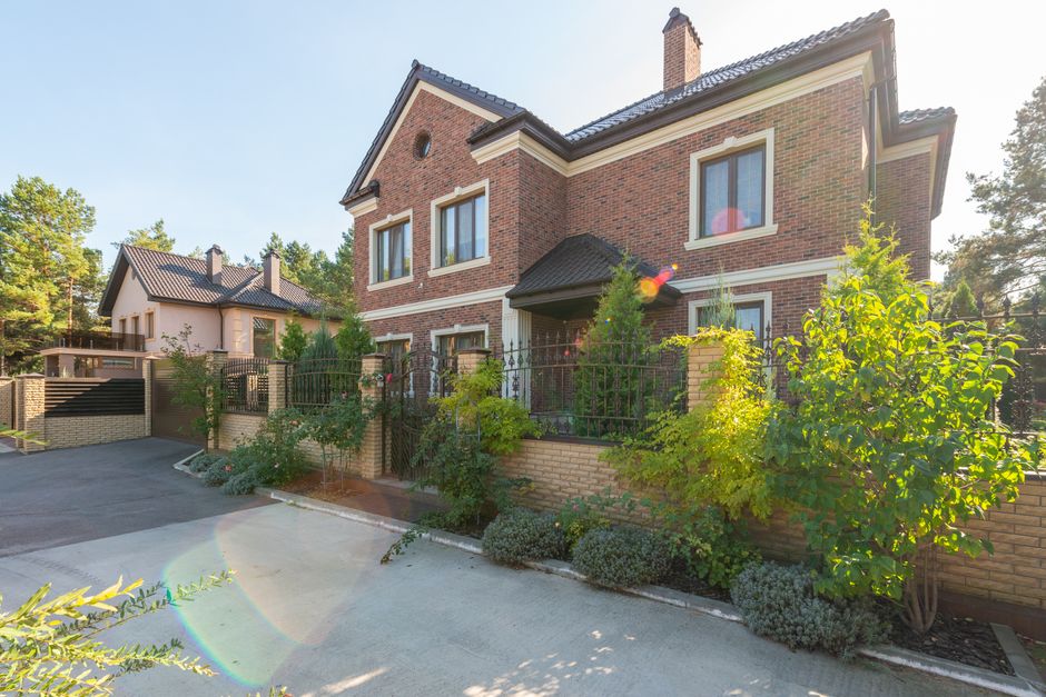 Elegant brick house with a lush garden and driveway, under a clear sky.