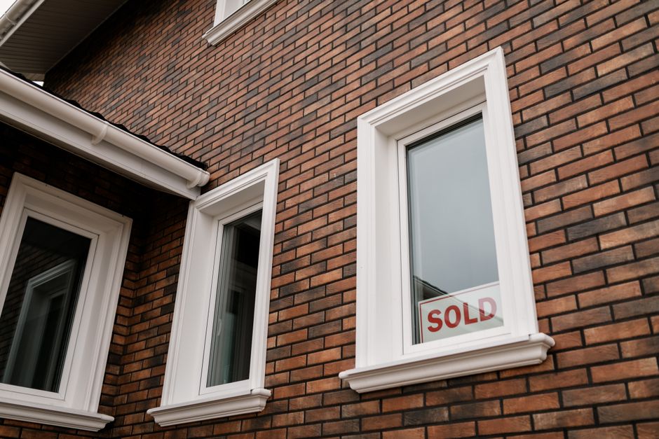 Close-up of a brick house with a ’Sold’ sign in the window, showcasing real estate sales.